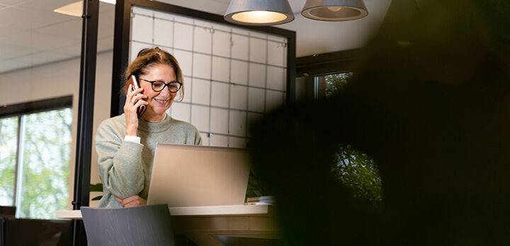 Vrouwelijke medewerker belt achter laptop op flexibele werkplek