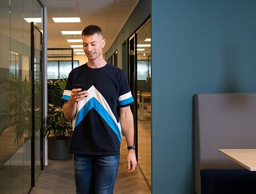 Medewerker die met zijn smartphone door een kantooromgeving loopt